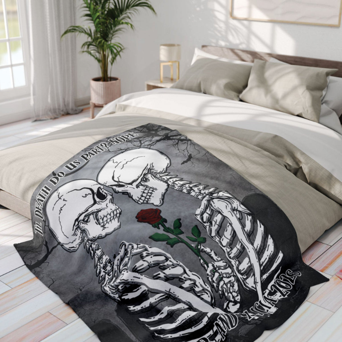 A printed blanket featuring two white skeletons facing each other with a red rose, draped over a bed in a bright, modern bedroom.
