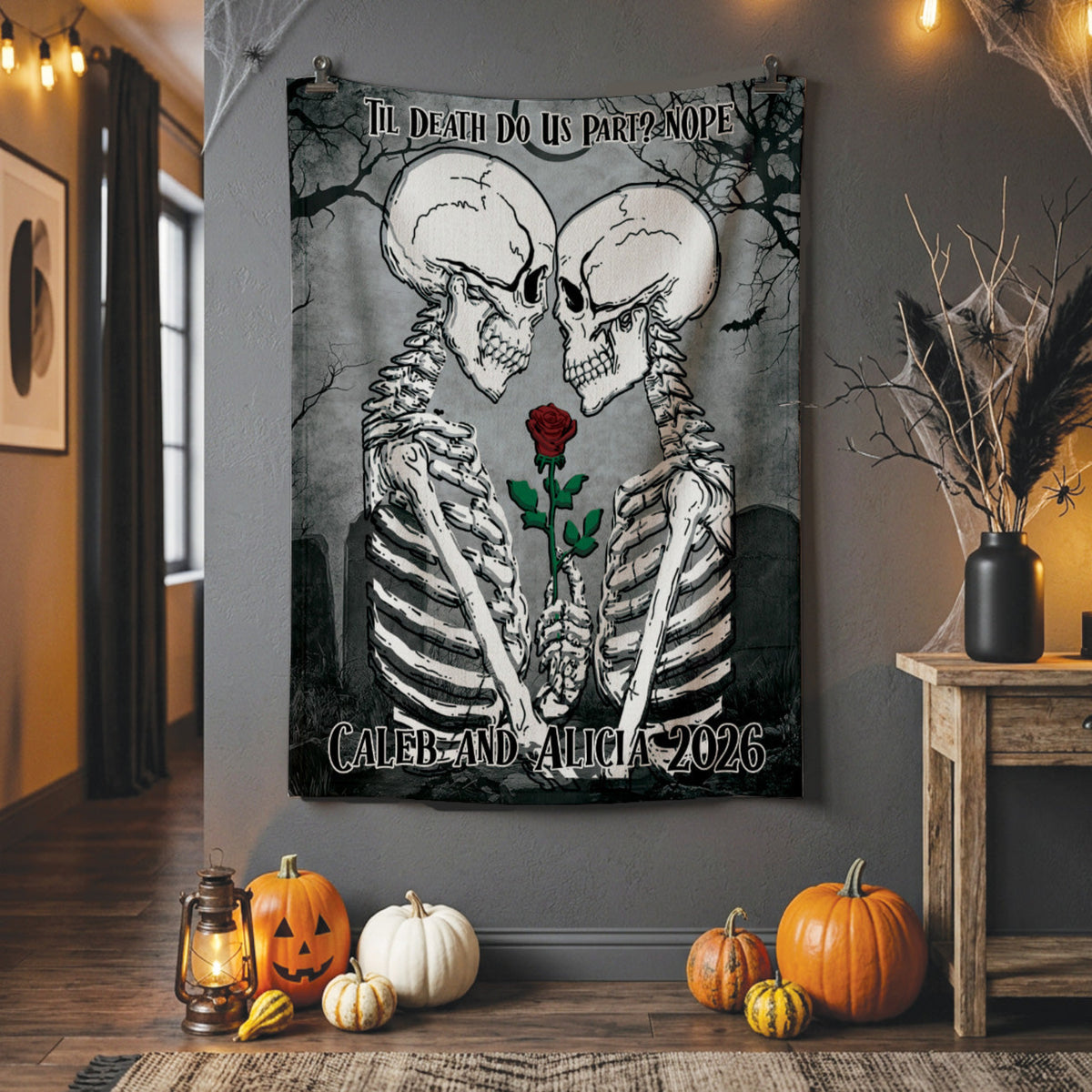 A Halloween-themed wall tapestry featuring two skeletons facing each other with a single red rose between them, displayed in a cozy room setting with pumpkins, a lantern, and a side table.