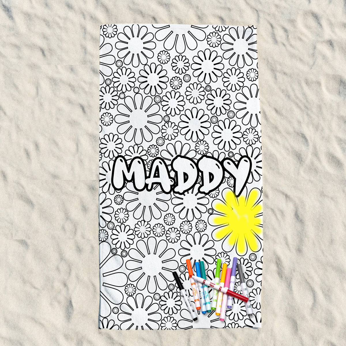 A personalized coloring book or art sheet with the name 'MADDY' in bold black letters, featuring a black and white daisy pattern on a textured light background, with a yellow flower and colored markers at the bottom.