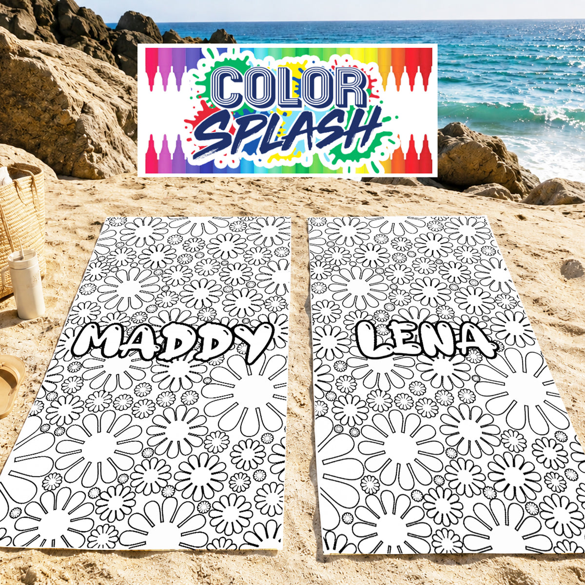 Two black-and-white floral coloring mats labeled 'MADDY' and 'LENA' laid on a sandy beach, with a colorful 'COLOR SPLASH' sign above and ocean rocks in the background.