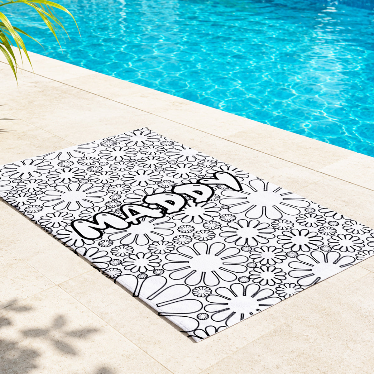 A rectangular outdoor mat with a black and white floral pattern and the word 'MADAY' across it, placed beside a swimming pool on a light stone deck.