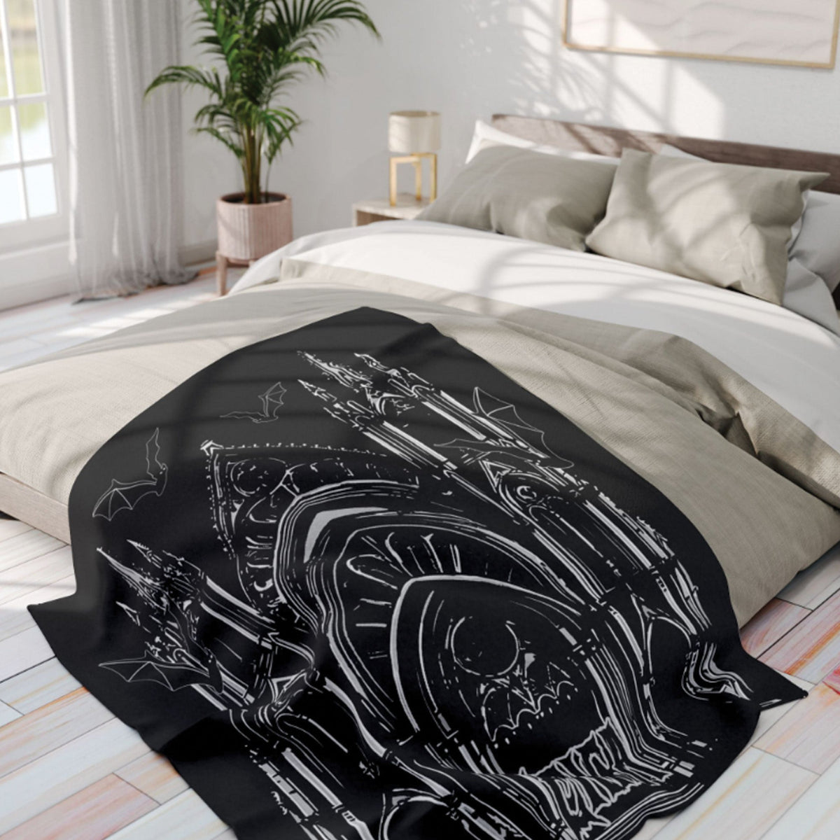 A black throw blanket with a white line-art gothic illustration of a cathedral and bats is draped over a bed in a bright, modern bedroom.