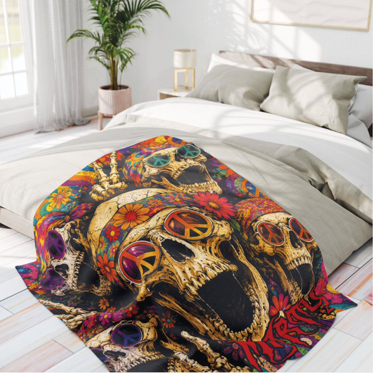 A colorful printed blanket featuring three gold-toned skulls with peace signs in their eyes, surrounded by bright flowers, draped over a bed in a modern bedroom setting.