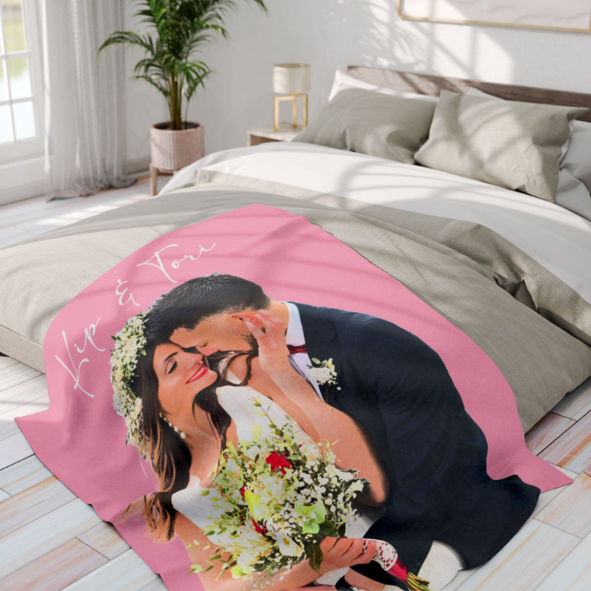 A custom printed blanket featuring a photo of a bride and groom kissing, styled on a bed in a bright, modern bedroom. The blanket has a pink background with the custom photo printed on it.