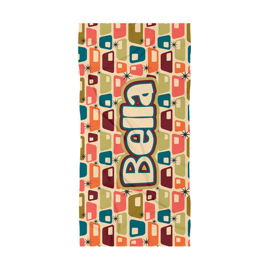A rectangular beach towel featuring a retro mid-century modern pattern of colorful retro cabins on a beige background, with the word 'BELLA' printed vertically in large retro-style lettering in the center.