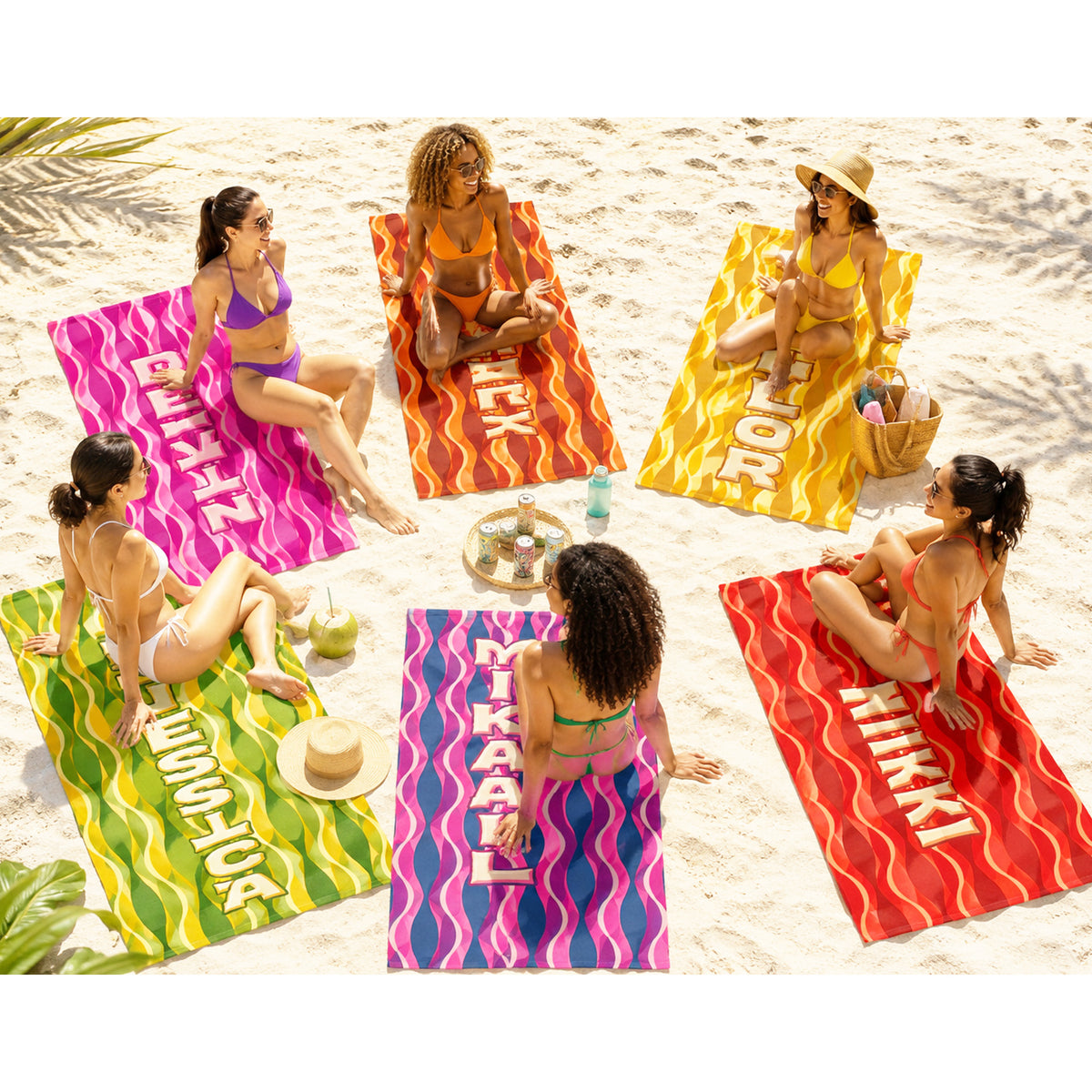 Six women in bikinis sit on colorful beach towels laid out on white sand. The towels feature bold wavy stripes and large white text reading names like BFF, FAVOR, MIKKI, and MIRACLE.