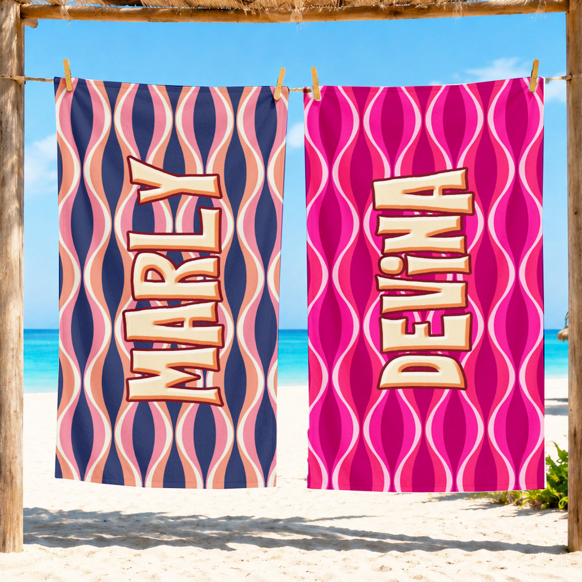 Two personalized beach towels hanging from a wooden frame at the beach, featuring retro wavy patterns and the names 'MARLY' and 'DEVINA' in large 3D letters.