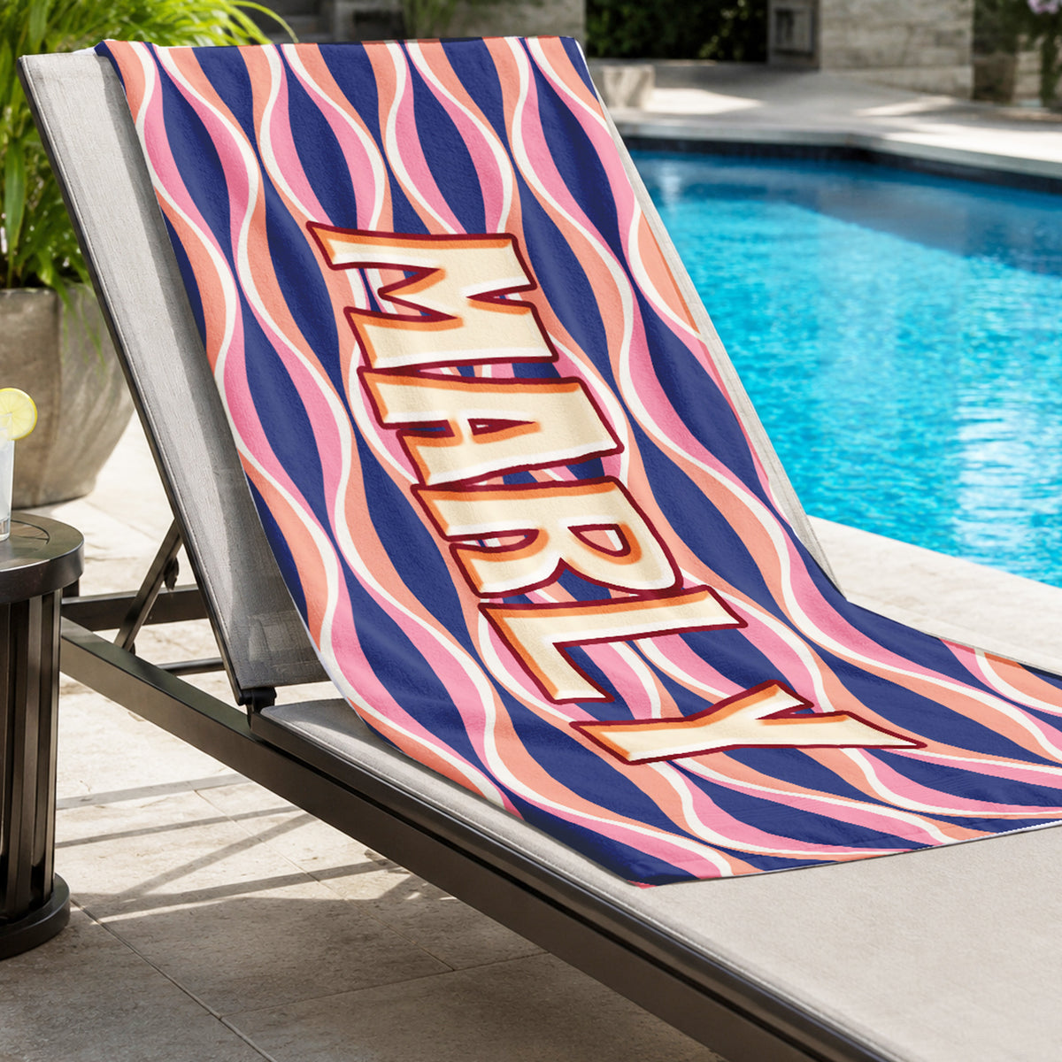 A rectangular beach towel featuring a retro wavy pattern in navy blue, pink, and peach, with the name 'MARLY' printed vertically in large beige block letters with a red outline.