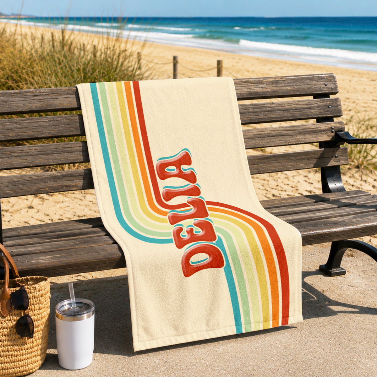 A cream-colored beach towel draped over a wooden bench at the beach, featuring retro vertical rainbow stripes in orange, red, yellow, green, and blue, with the word 'BELIEVE' printed in large red letters.
