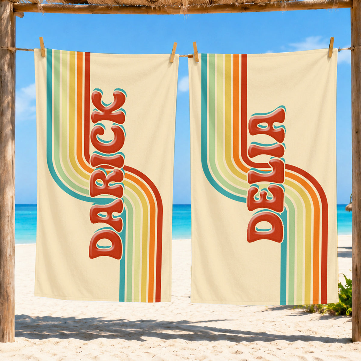 Two cream-colored beach towels hanging on a wooden stand at a beach. Each towel features retro vertical text reading 'DARICK' and 'DELTA' in red with teal and orange outlines, alongside retro wavy stripes in teal, green, yellow, orange, and red.