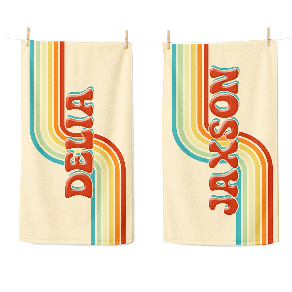 Two cream-colored towels hanging from a string with wooden clothespins, featuring retro vertical rainbow stripes and the names 'DELTA' and 'JAXON' in red-orange lettering with teal outlines.
