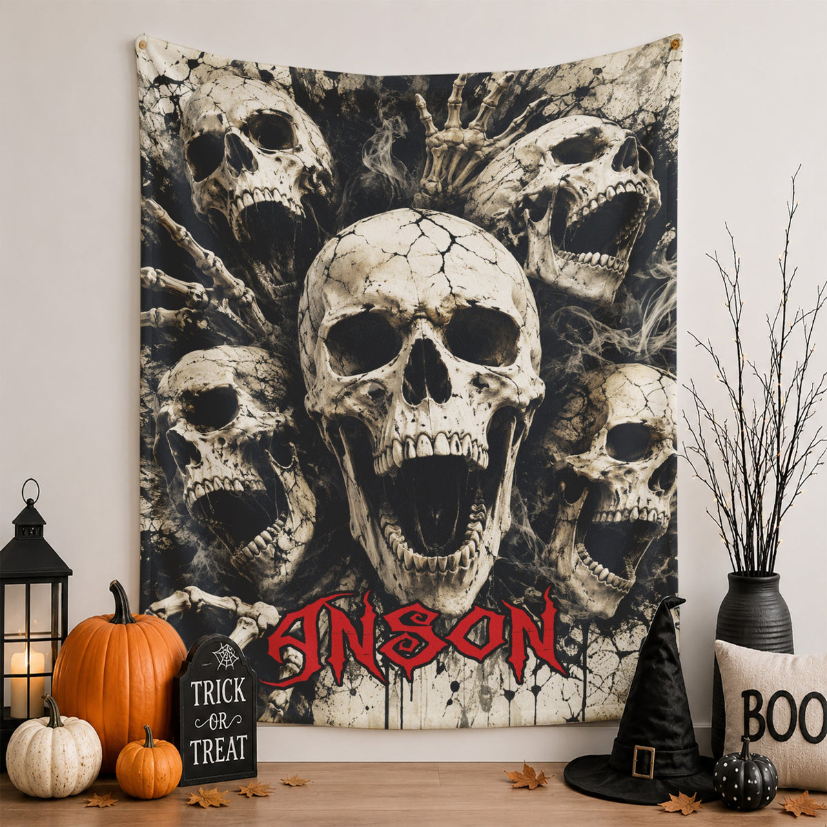 A Halloween-themed wall tapestry featuring a large central skull surrounded by smaller skulls, skeletal hands, and the word 'CARNATION' in red gothic lettering. The tapestry is displayed on a wall in a styled room setting with pumpkins, a lantern, a black witch hat, and a decorative vase.