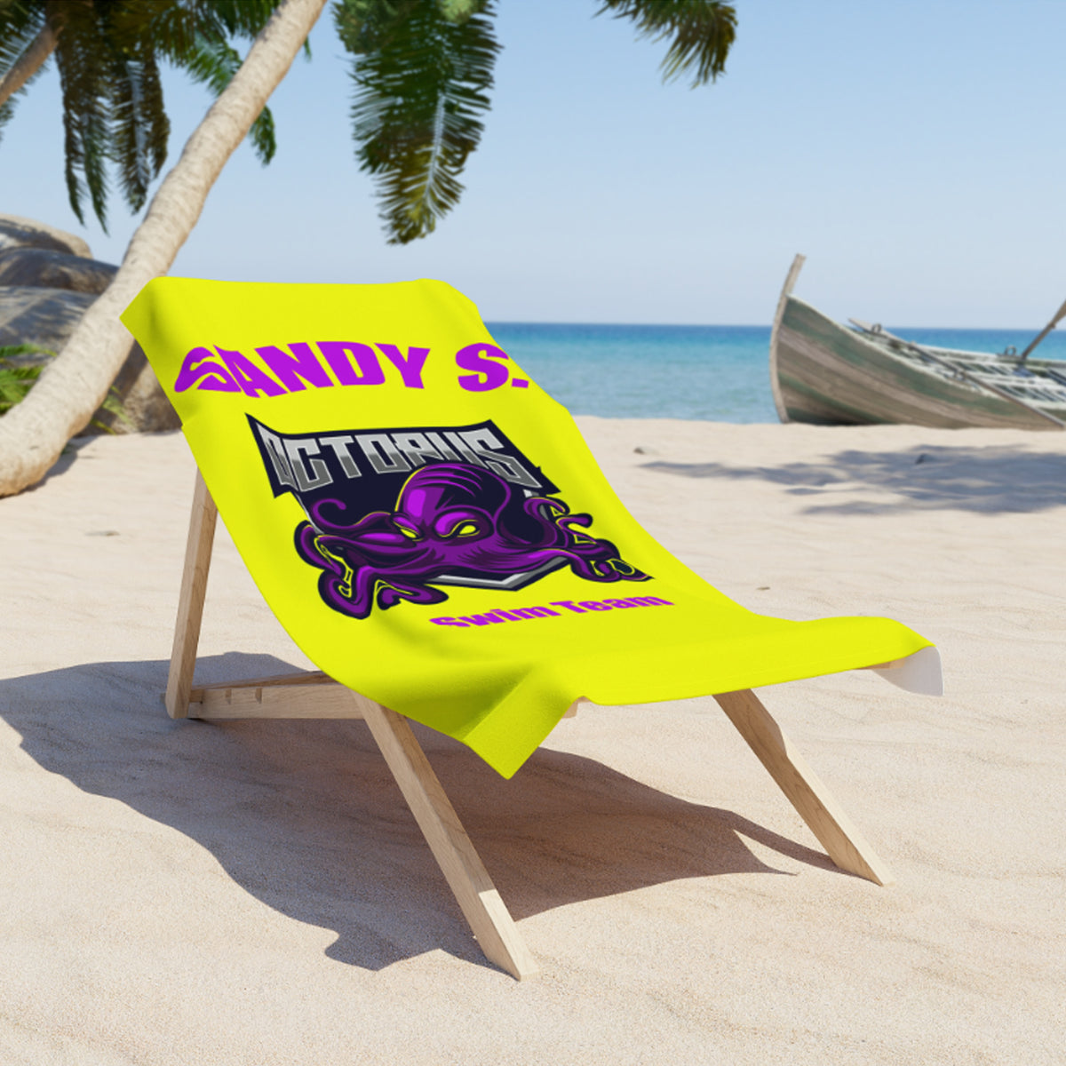 A bright yellow beach towel with a purple octopus graphic and pink text reading 'ANDY S. OCTAGON' is draped over a wooden beach chair on a sandy beach with palm trees and the ocean in the background.