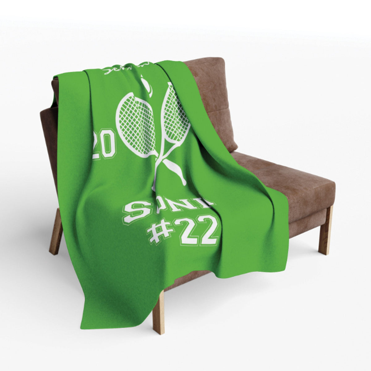 A bright green throw blanket with a white tennis racket graphic and the text 'SINCE #22' draped over a brown armchair against a light gray background.