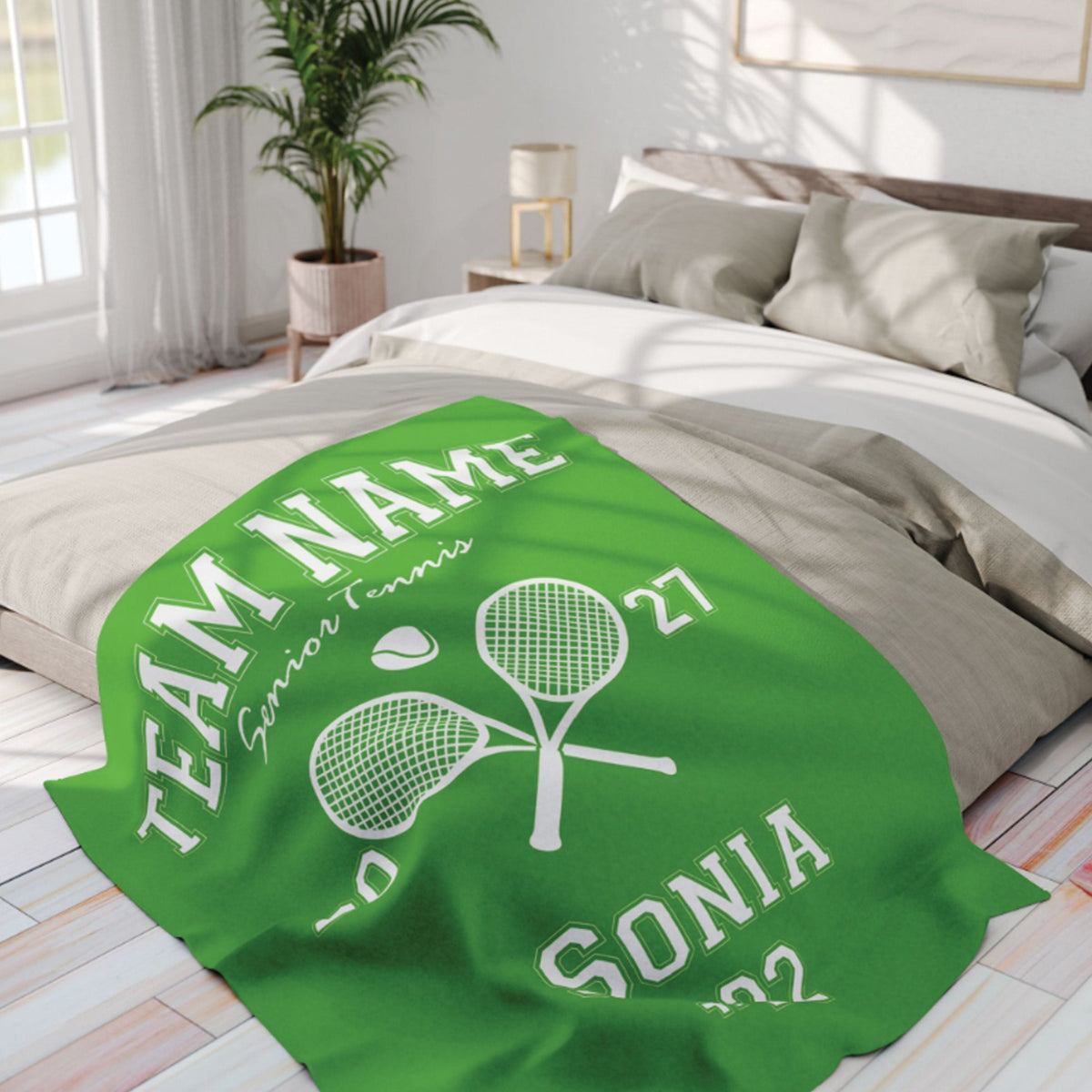 A bright green personalized blanket with white tennis-themed text and crossed tennis rackets is draped over a bed in a modern, sunlit bedroom.