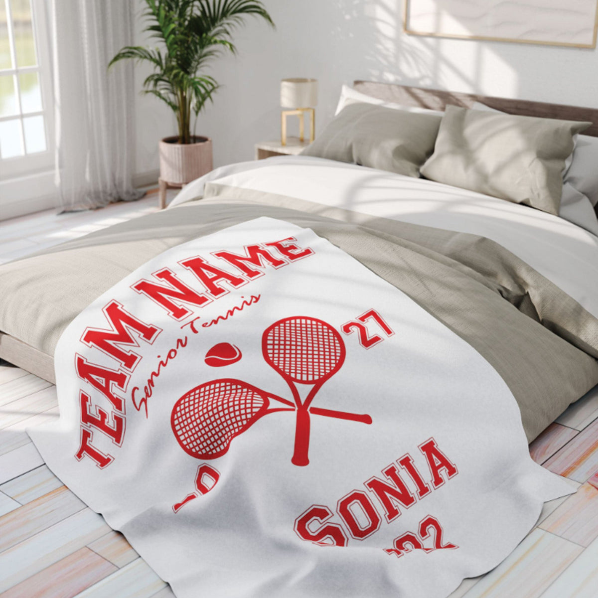 A white personalized blanket with a red tennis-themed graphic and text, draped over a bed in a bright, modern bedroom.