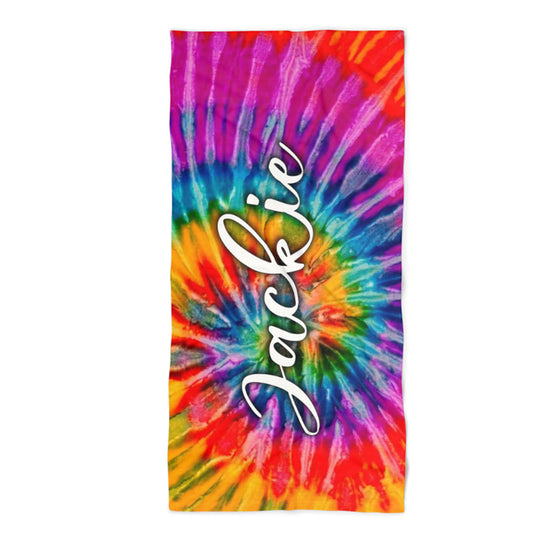 A rectangular beach towel featuring a vibrant rainbow tie-dye spiral pattern with the name 'Jackie' printed vertically in white cursive script in the center, shown against a plain white background.