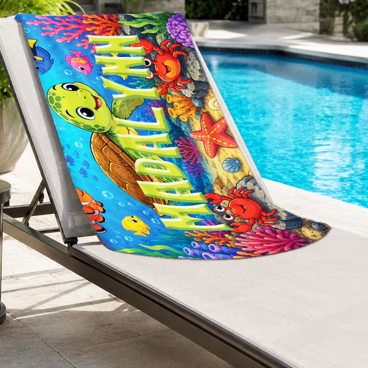 A colorful beach towel featuring cartoon sea turtle, crab, starfish, and coral reef illustrations, draped over a white outdoor lounge chair beside a swimming pool.