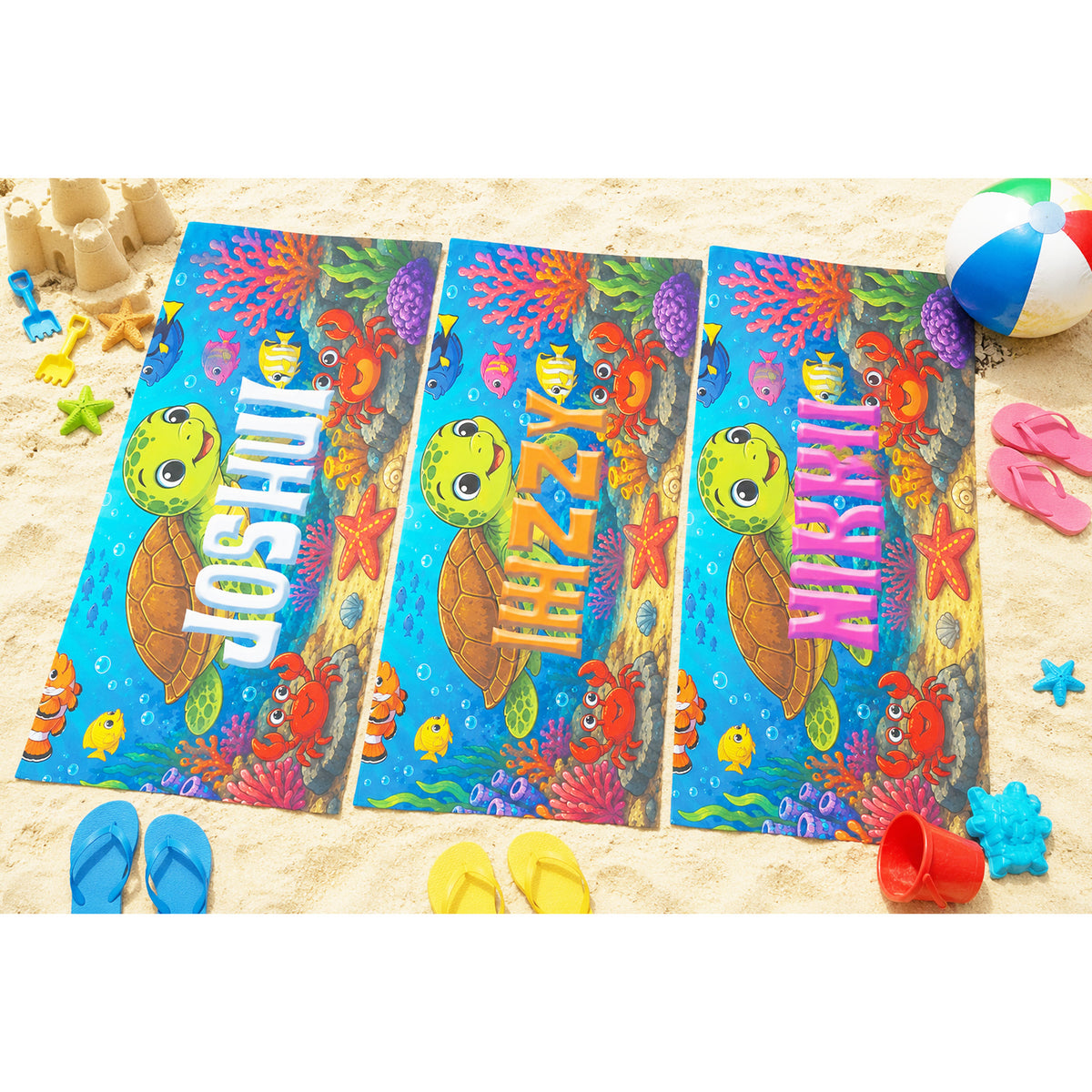 Three personalized beach towels laid out on sand, each printed with a colorful underwater scene featuring a sea turtle, coral, fish, and large customizable names in 3D-style lettering. Blue, yellow, red, and pink beach accessories are scattered around them.