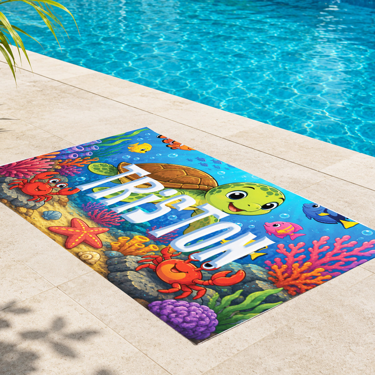 A colorful custom poolside mat featuring an underwater scene with the name 'TRISTON' in large white letters, shown on a beige tiled pool deck next to a swimming pool.