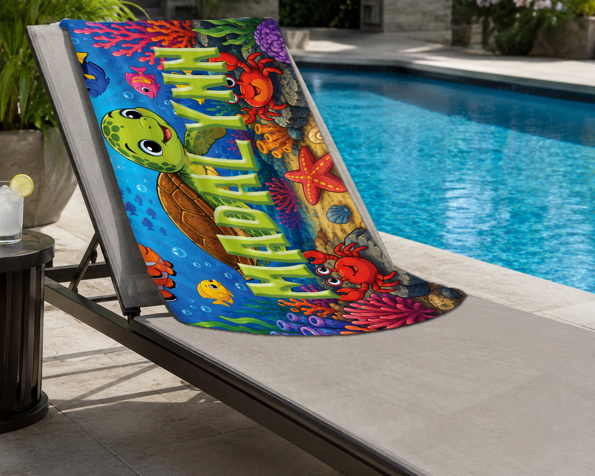 A colorful beach towel featuring an underwater scene with a green sea turtle, red crab, starfish, coral, and large vertical text reading 'WANDERER', draped over a patio lounge chair beside a swimming pool.