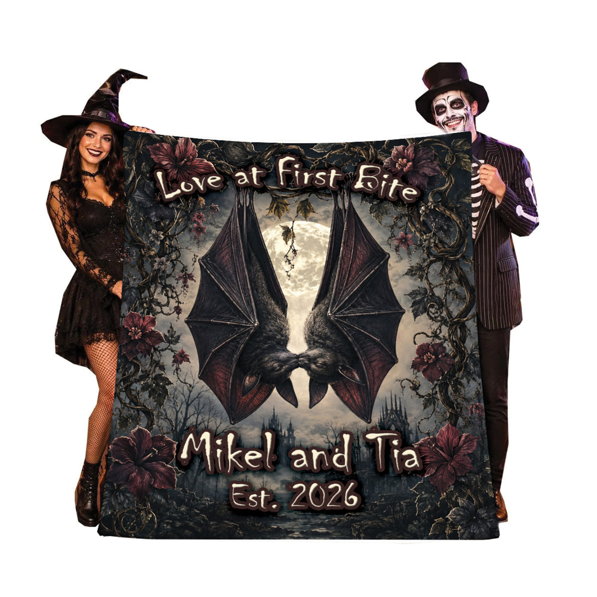 A custom gothic-themed blanket featuring a large bat, roses, and the text 'Love at First Bite' and 'Mikel and Tia Est. 2026', held up by a woman in a witch costume on the left and a man in a skeleton costume on the right against a white background.