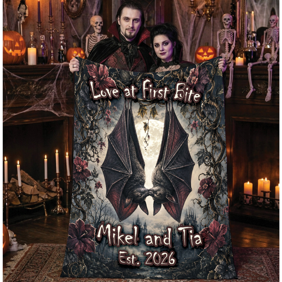 A couple holds up a large personalized Halloween blanket in a spooky, decorated room. The blanket features a gothic illustration of two bats facing each other, surrounded by dark roses and vines, with the text 'Love at First Bite' at the top and 'Mikel and Tia Est.