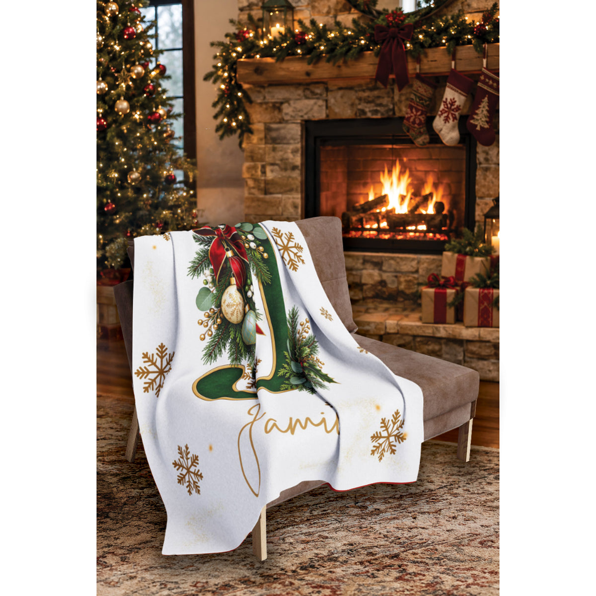 A personalized Christmas-themed throw blanket draped over a gray armchair in a cozy living room setting with a fireplace, stockings, and a decorated tree in the background. The blanket is white with a large green letter 'J', gold snowflakes, a green stocking illustration, and the name 'Jami' in gold script.