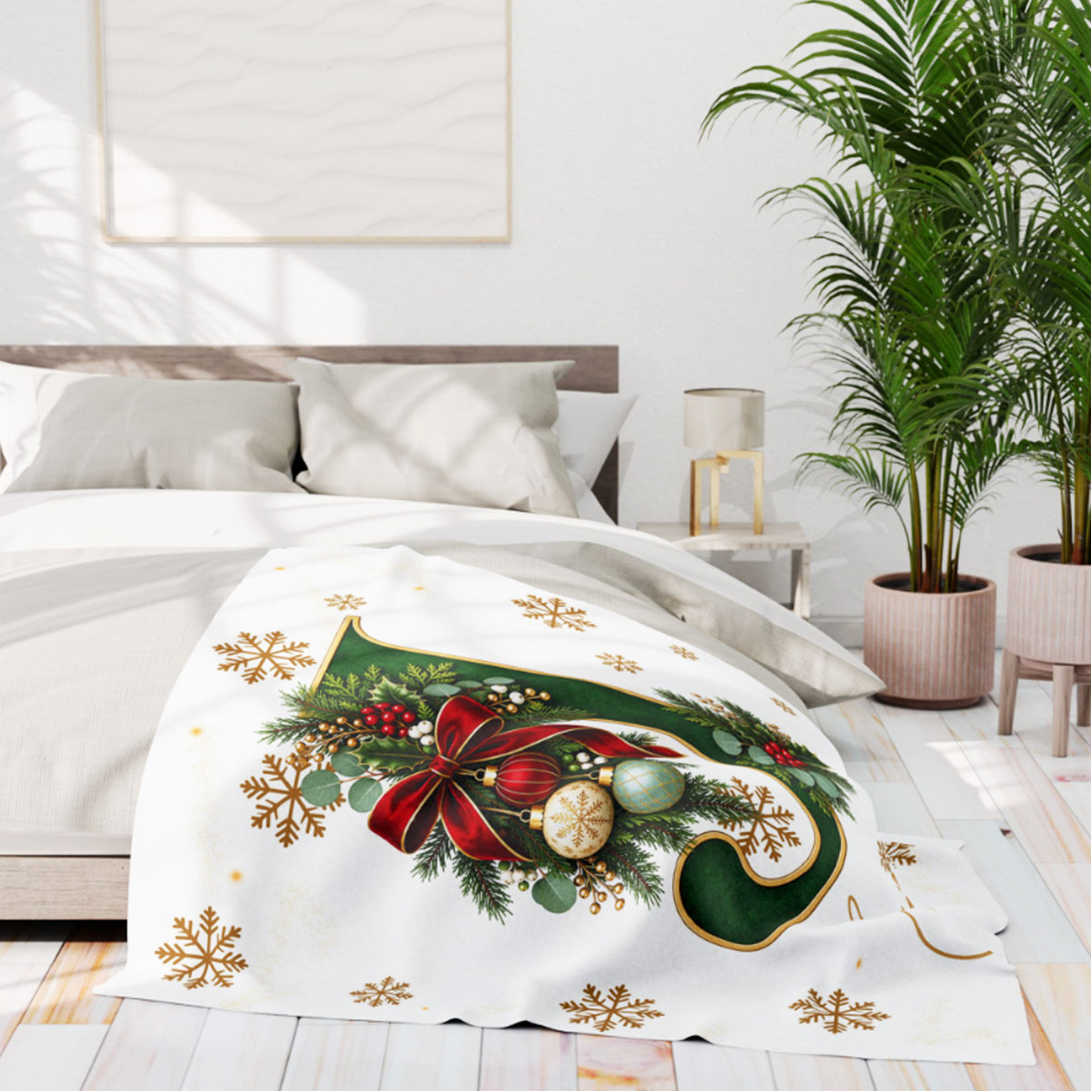 A white Christmas-themed throw blanket draped over a bed in a bright, modern bedroom. The blanket features a large green stocking design decorated with a red bow, gold snowflakes, green pine branches, and red berries, with smaller gold snowflakes scattered around the border.